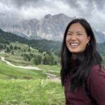 Grace smiling with her black hair down, in front of a mountain landscape.
